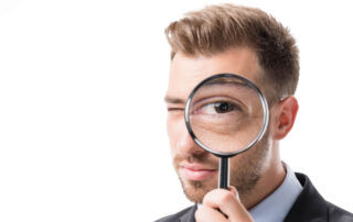 man holding magnifying glass to eye